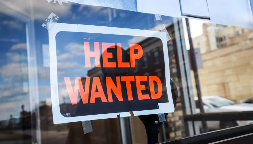 “Help Wanted” sign taped to a glass door, indicating restaurant or business hiring.