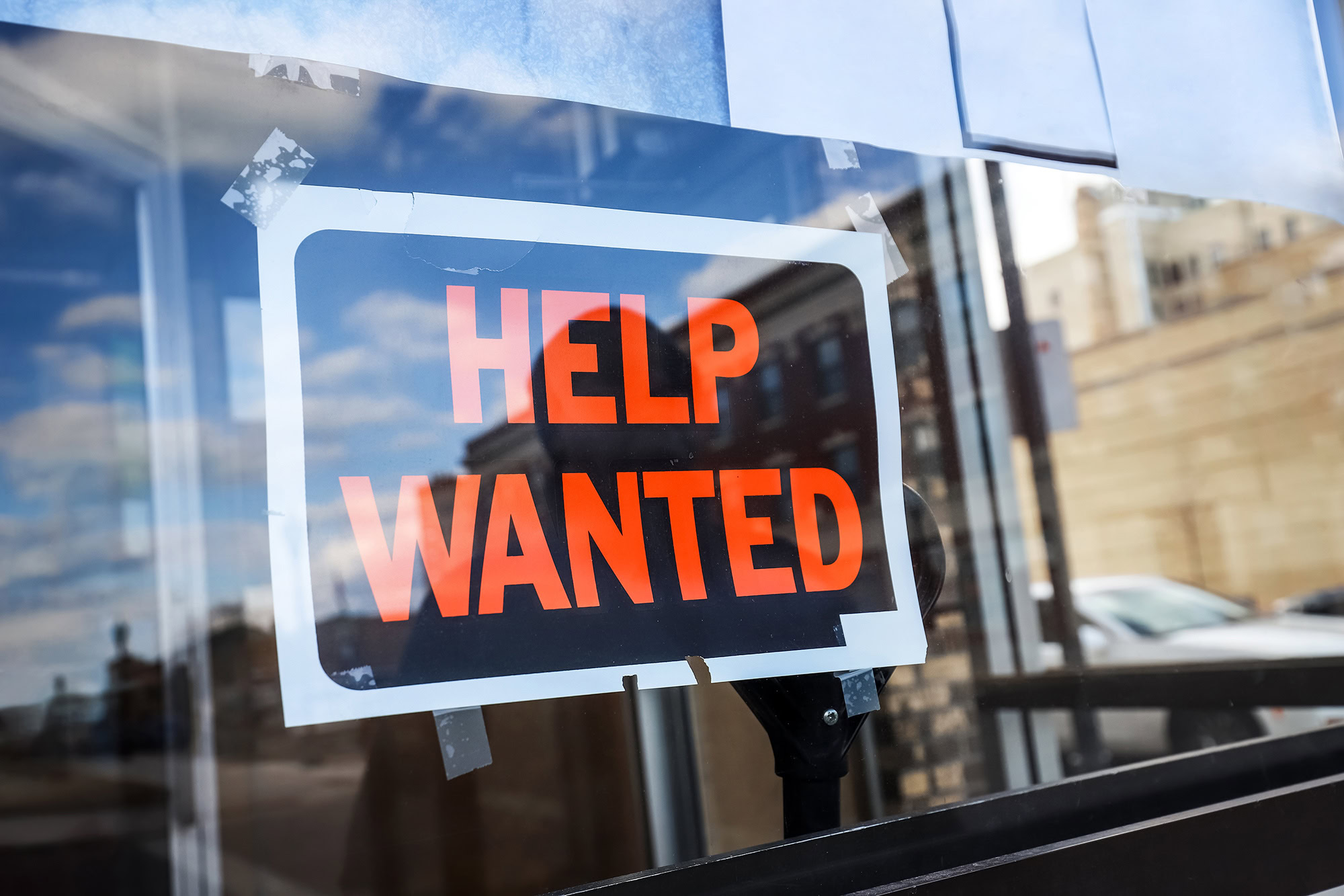 “Help Wanted” sign taped to a glass door, indicating restaurant or business hiring.